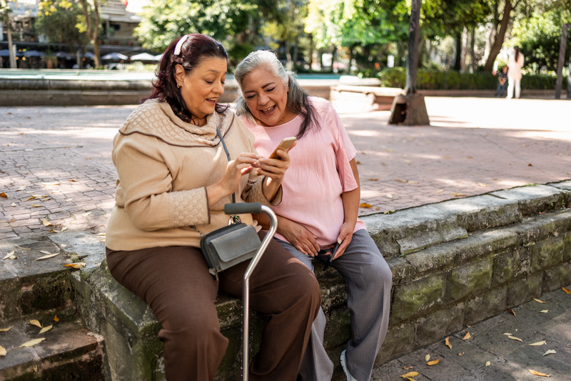Two senior Hispanic women using mobile phone - stock photo
Two old women sitting at the park and using mobile phone