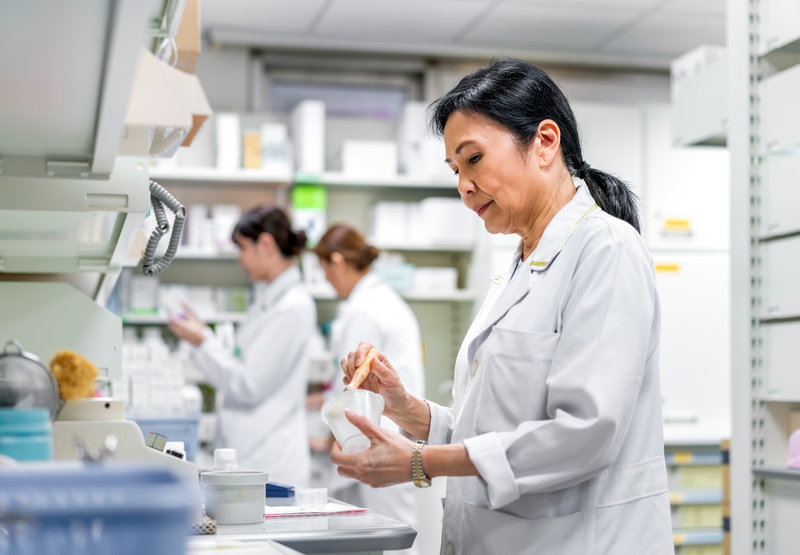 Side view of mature pharmacist working in store - stock photo
Mature pharmacist working in store with coworkers in background. Confident female medical worker holding medical equipment at desk. She is in hospital.