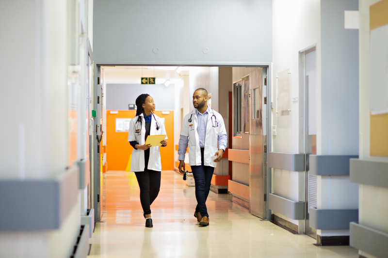 Doctors walking in hospital corridor - stock photo
A male and female young African doctors walking down a hospital corridor talking. There is blank copy space in the image.