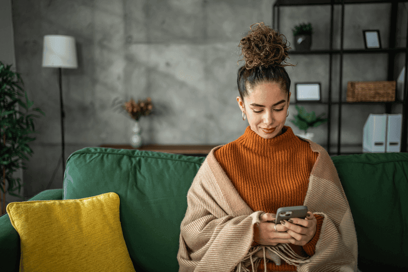 Portrait of cheerful woman using smart phone at home texting or surfing internet