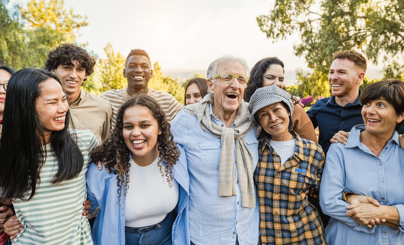 Group of multigenerational people smiling in front of camera - Multiracial friends of different ages having fun together - Main focus on caucasian senior face